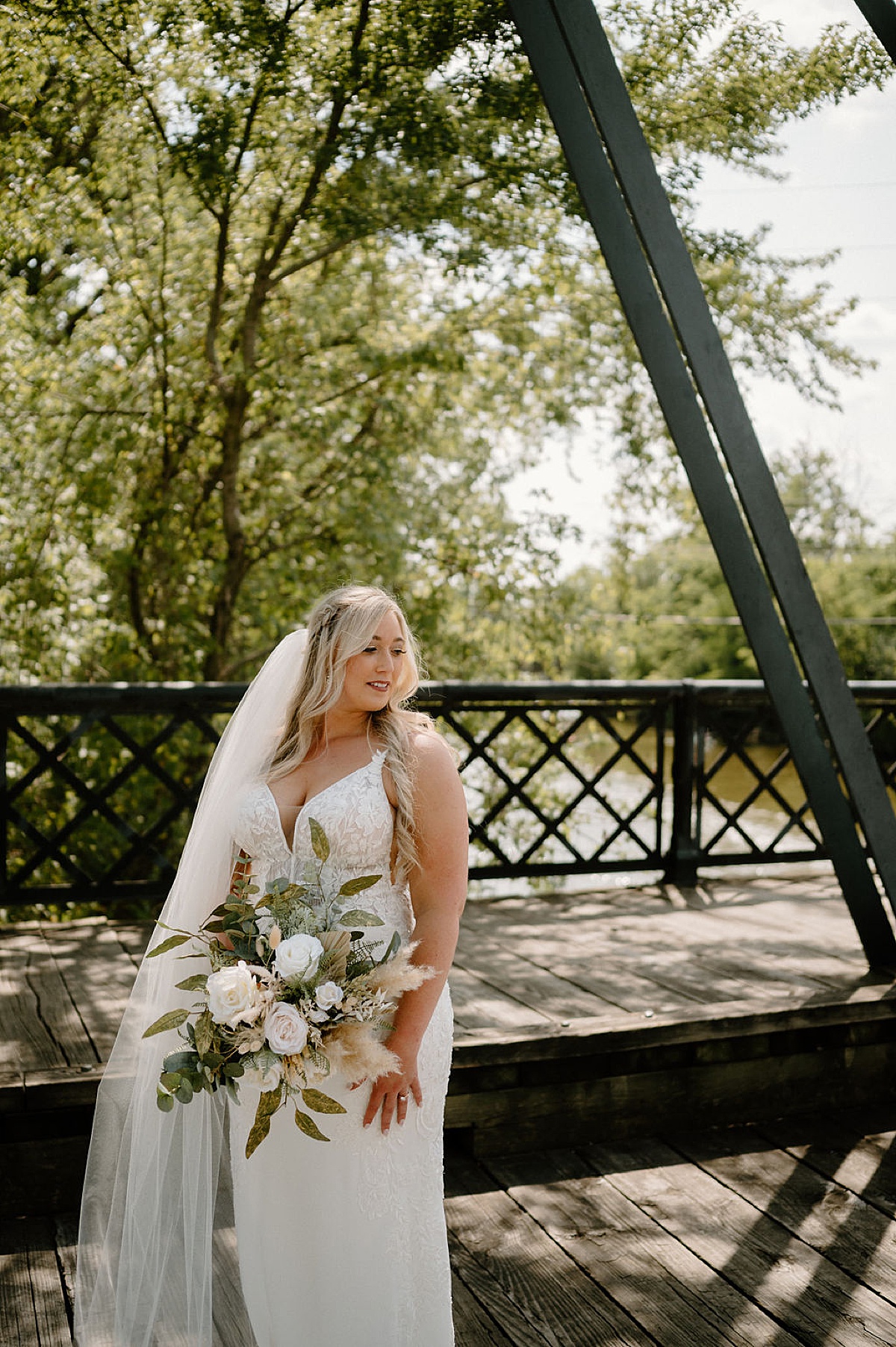 bride in boho lace wedding gown and boho bouquet with pampas grass poses on trestle bridge during photoshoot with midwest wedding photographer