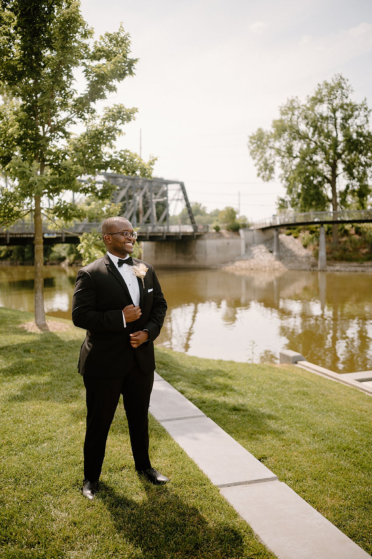 dapper groom with pampas grass boutonnière poses by the waterfront during photoshoot with midwest wedding photographer