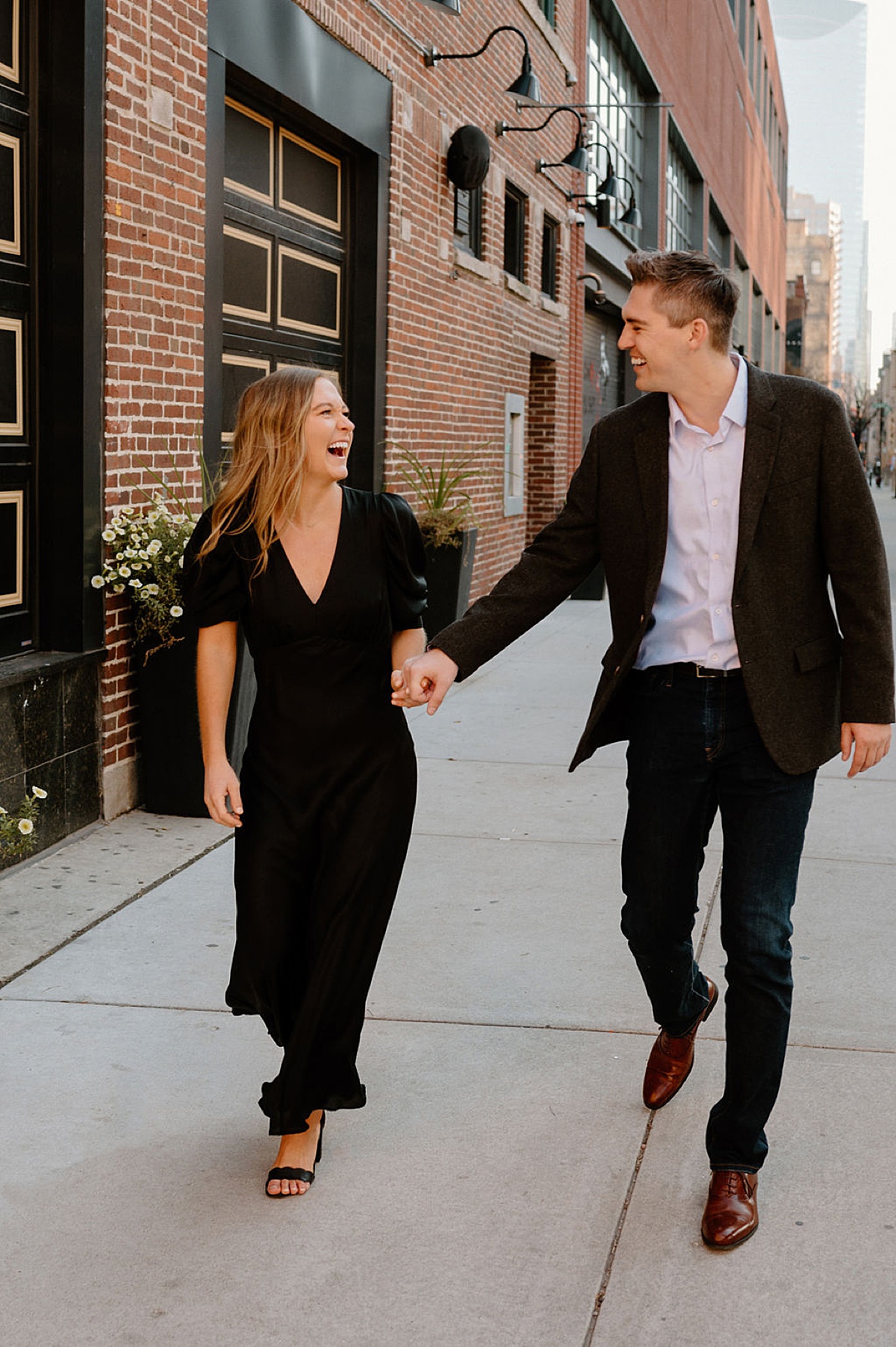 Millennial couple stroll a brick wall street while holding hands during engagement shoot with Chicago wedding photographer