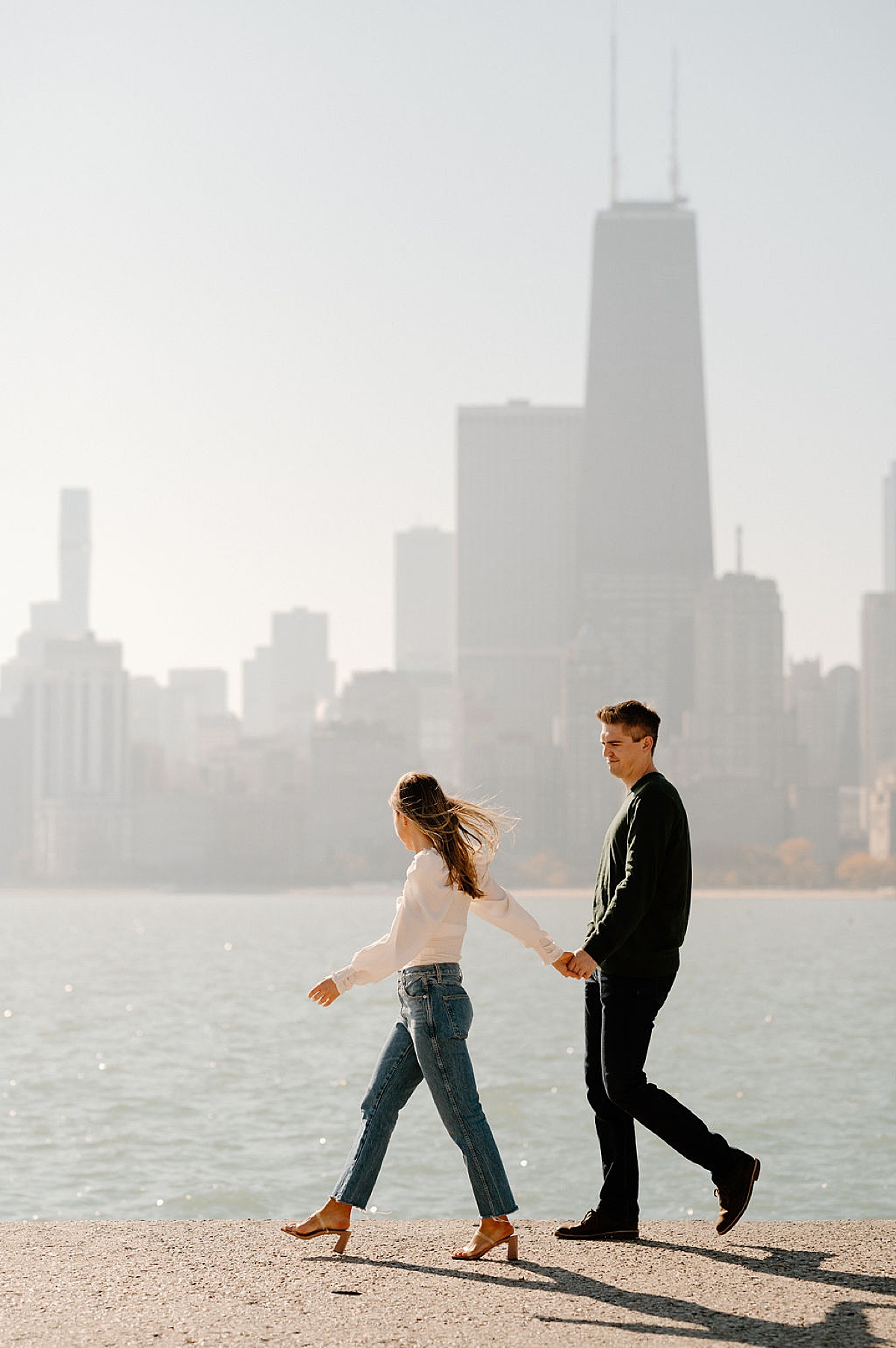cute classy couple walk along waterfront with Chicago skyline in the background during shoot with Indigo Lace Collective