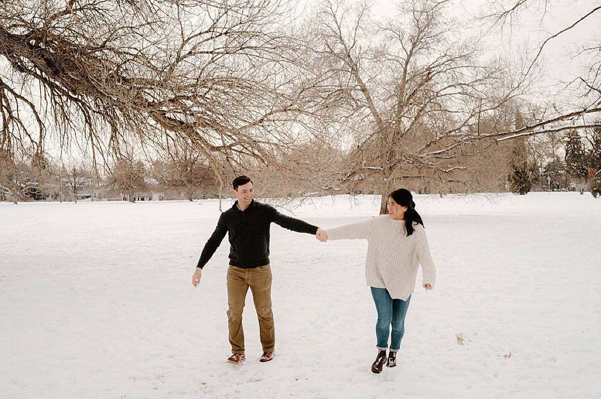 engaged man and woman dance hand in hand during snowy Cheesman Park engagement session
