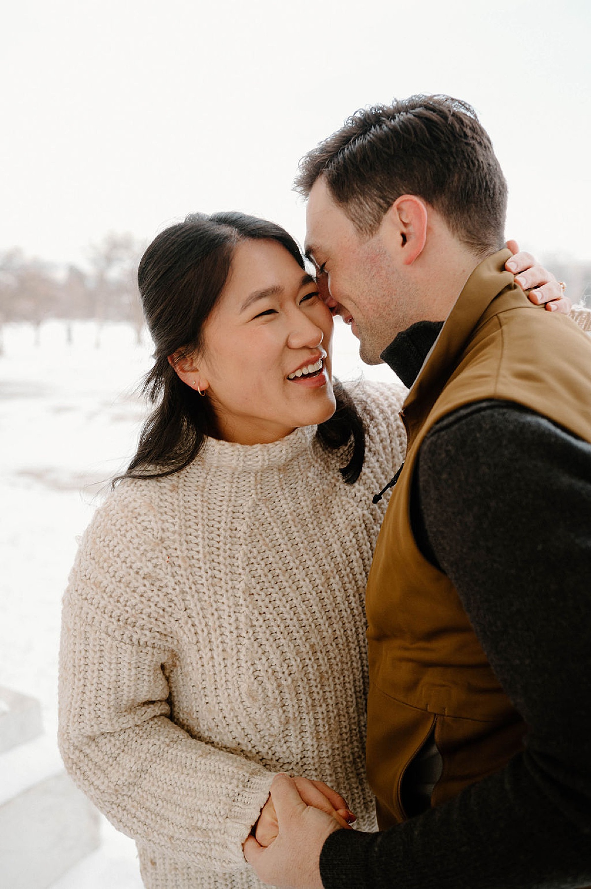 cute couple in sweaters and vest laugh during snowy Cheesman Park engagement session