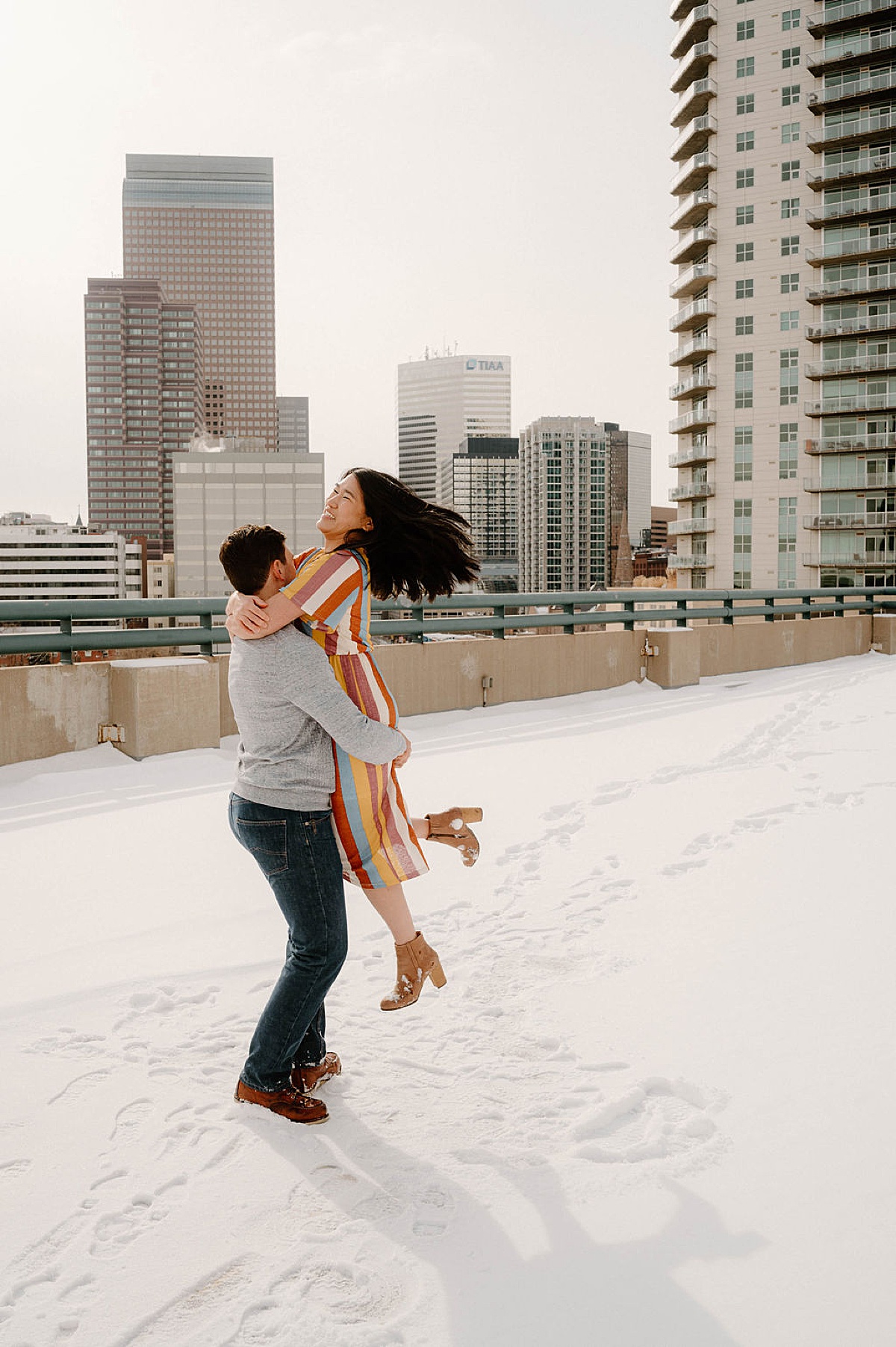 hip couple twirl on snowy rooftop during photoshoot with Denver wedding photographer