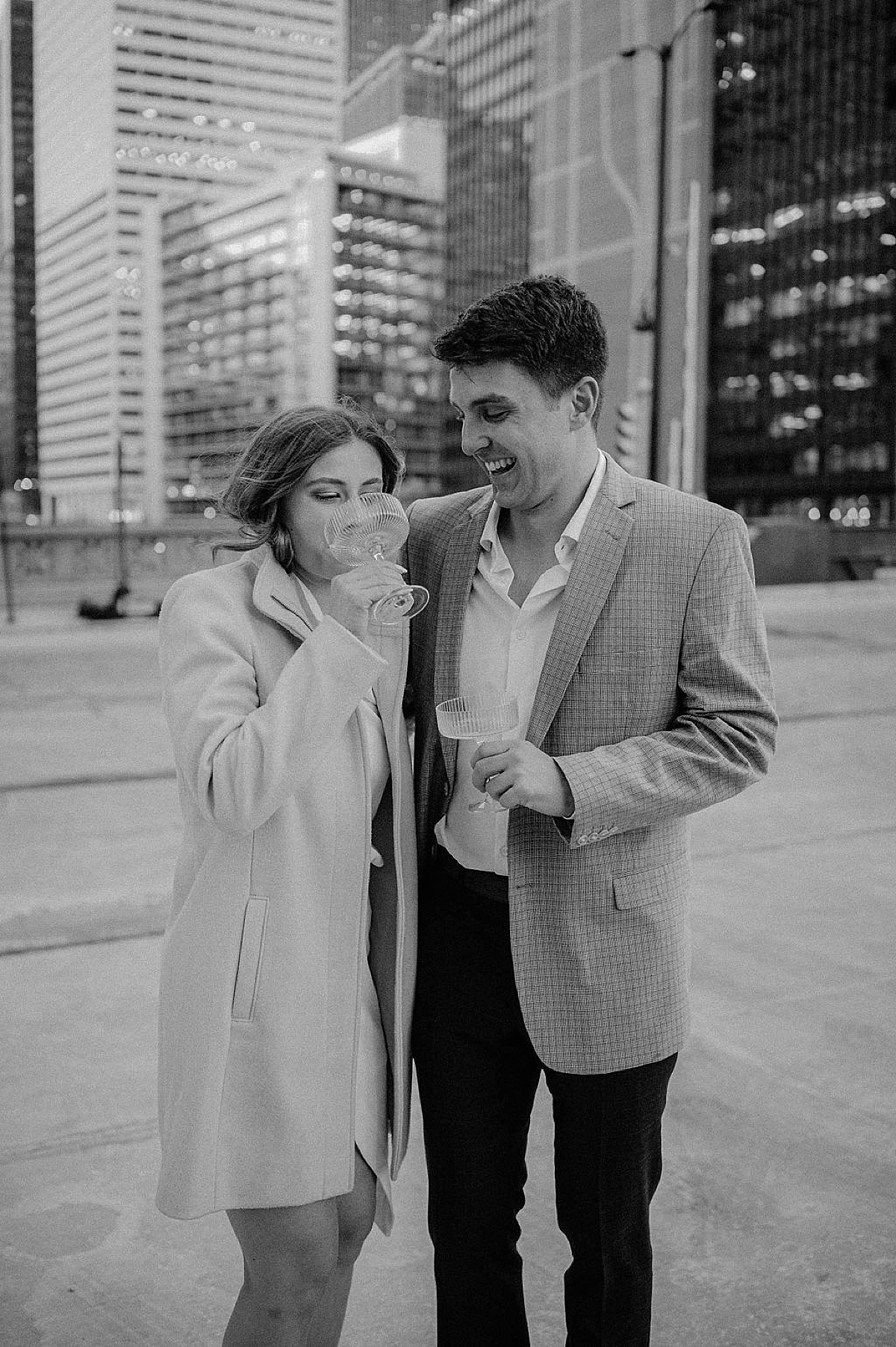 man and woman in classy jacket and knee length coat sip champagne after engagement shot by Indigo Lace Collective