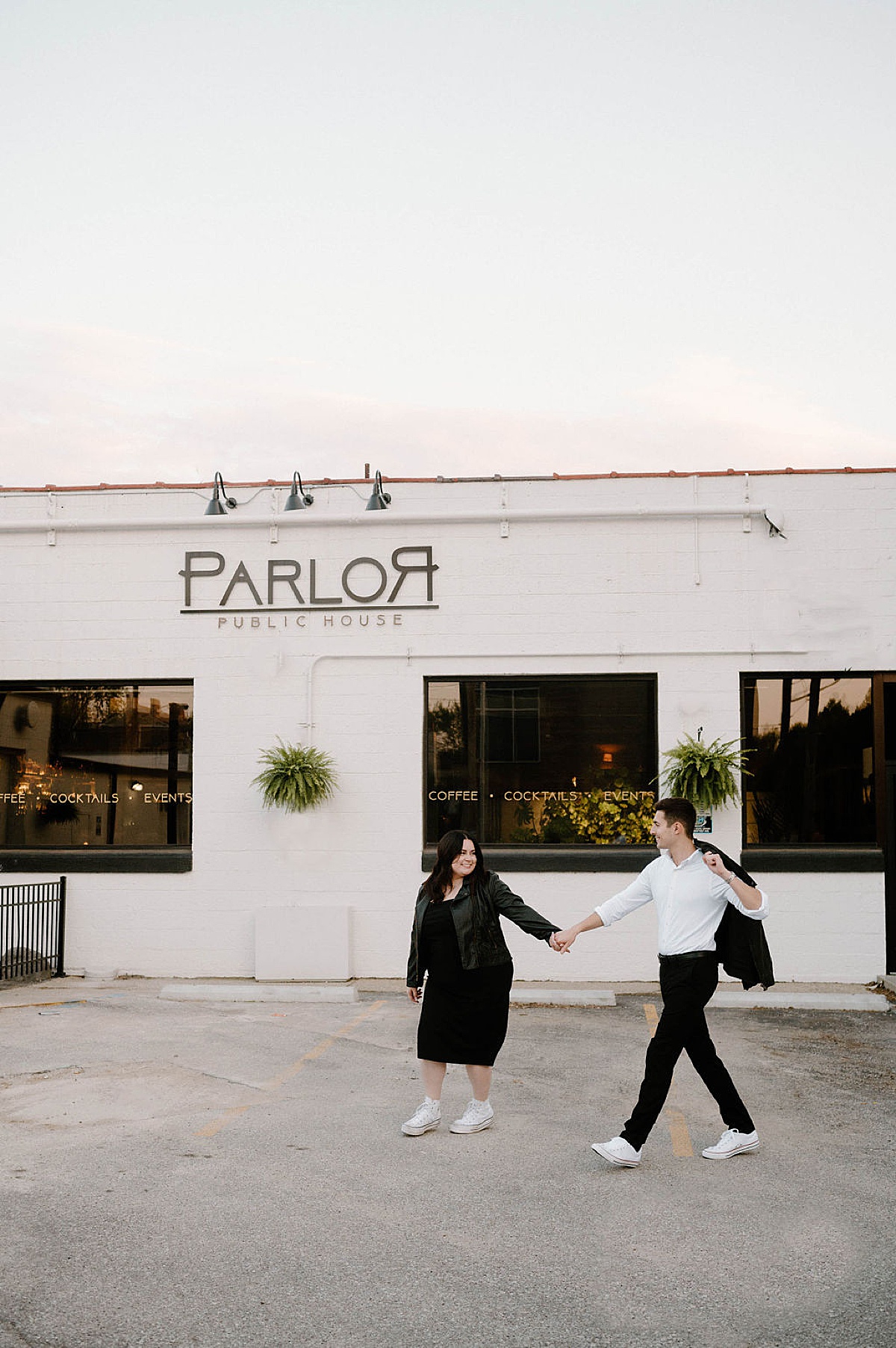 Cute couple in street clothes and matching sneakers pose in front of favorite restaurant during shoot with Midwest wedding photographer