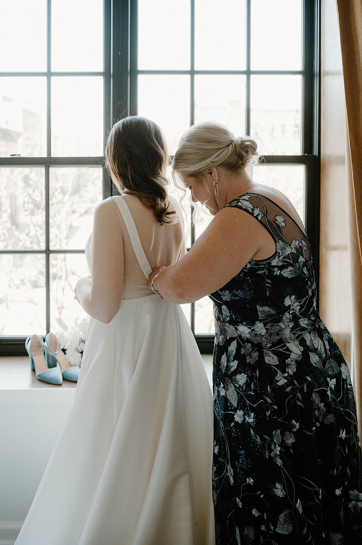 bride has help getting ready and fastening back of bridal gown before spring wedding at Artifact Events