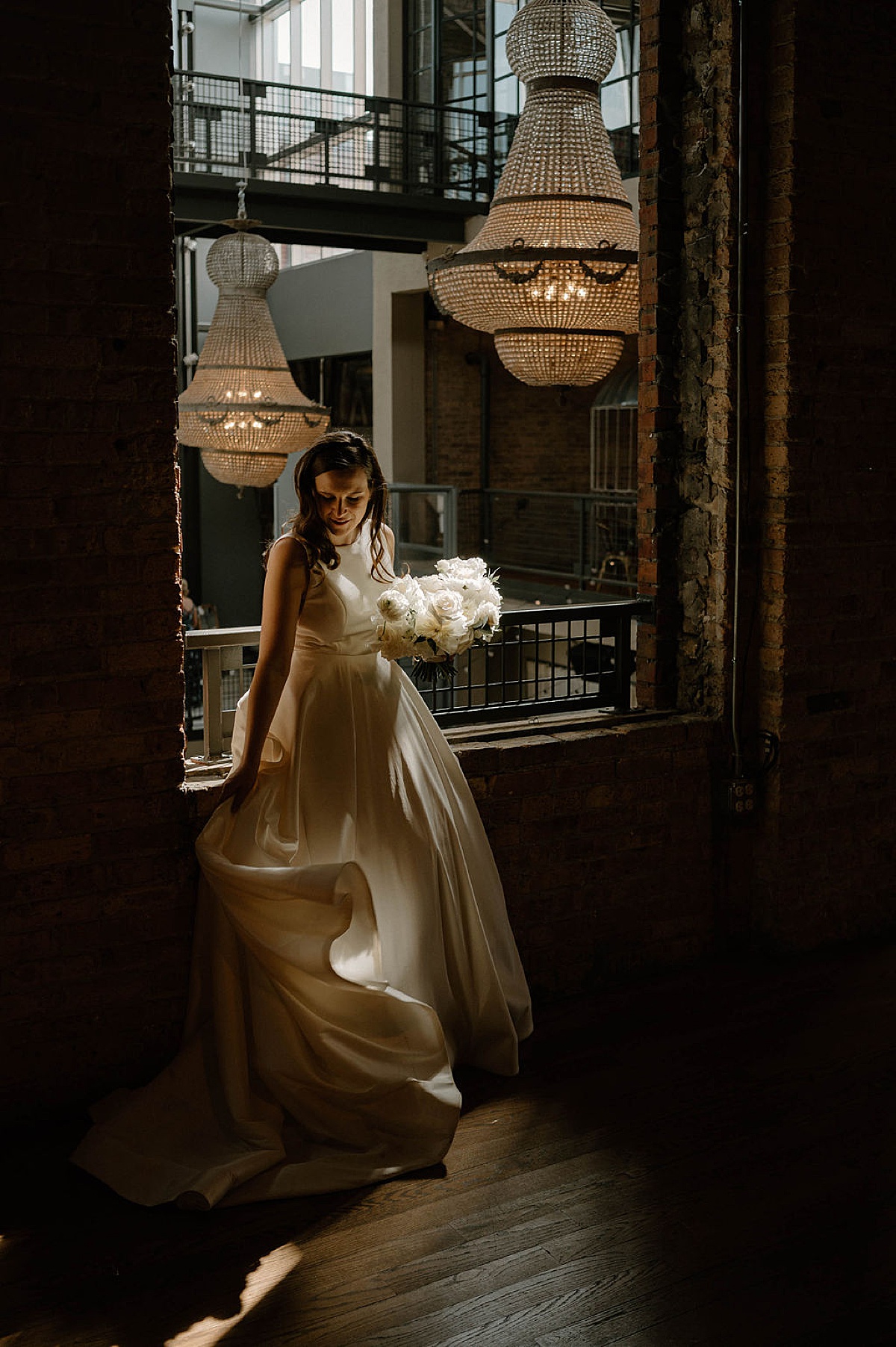 bride in white poses in moody industrial venue with gorgeous chandeliers shot by Chicago Wedding photographer
