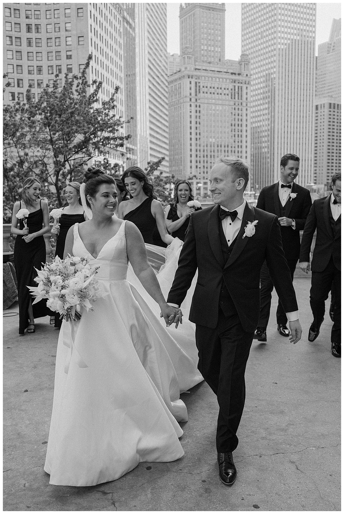 newlyweds walk down sidewalk followed by bridesmaids and groomsmen by Chicago photographer