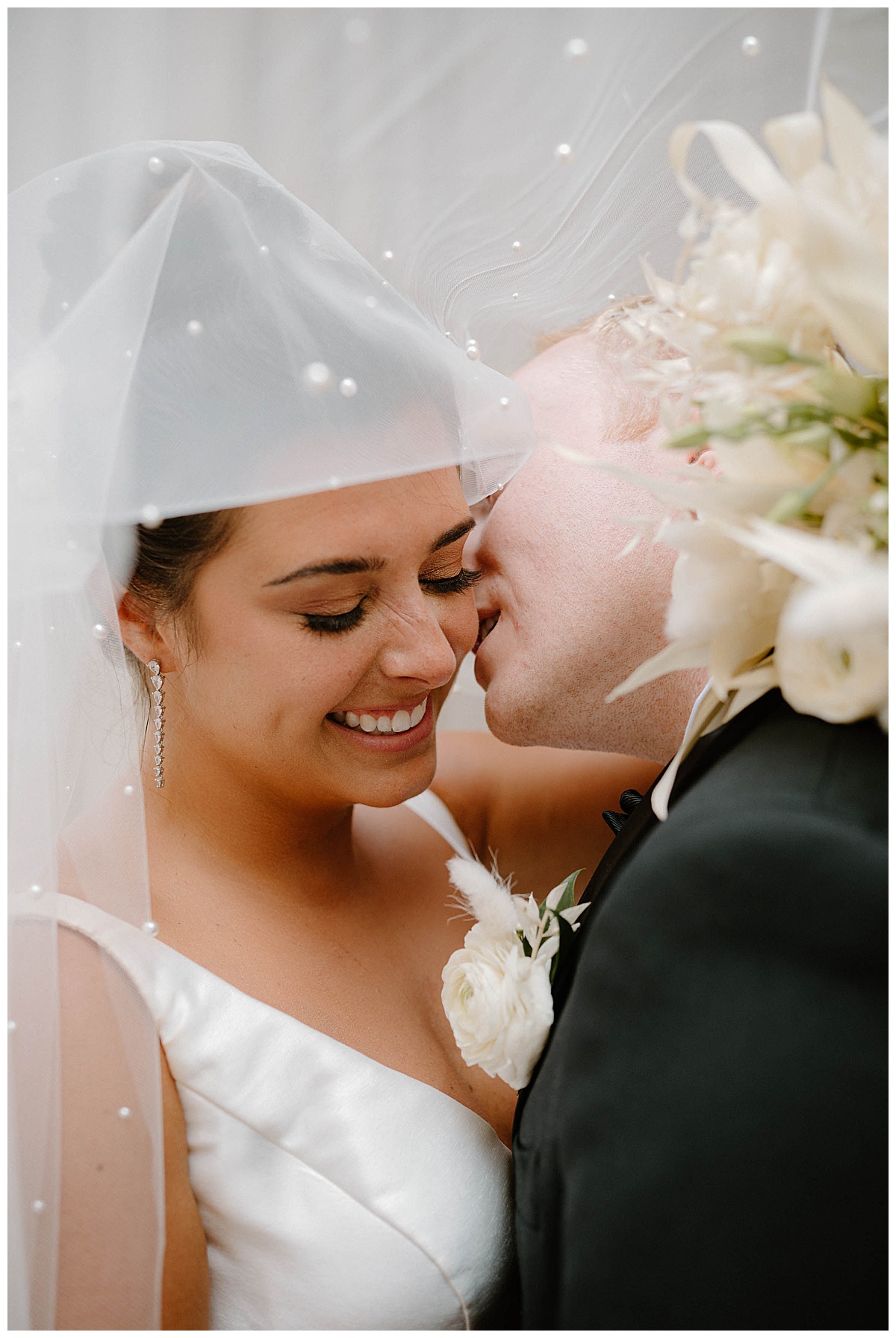 groom leans in to kiss bride's cheek under veil at Bridgeport Art Center wedding