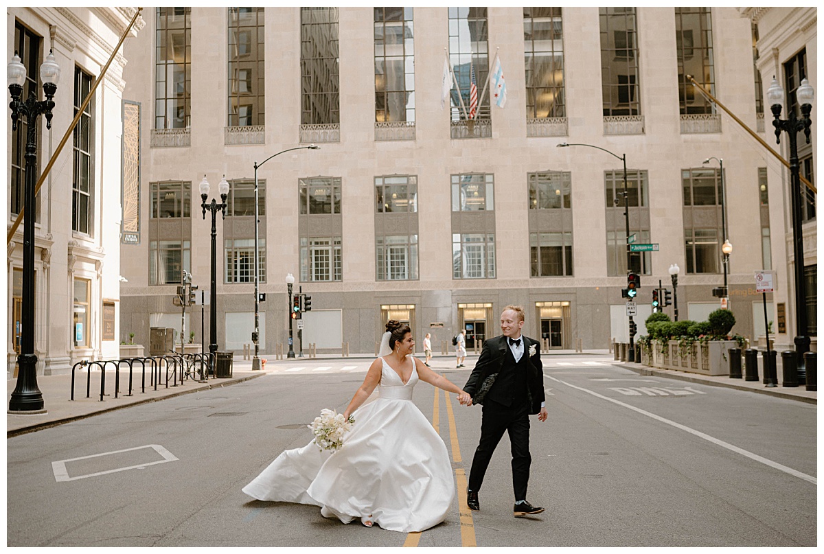 groom leads bride across the street by the hand by Indigo Lace Collective