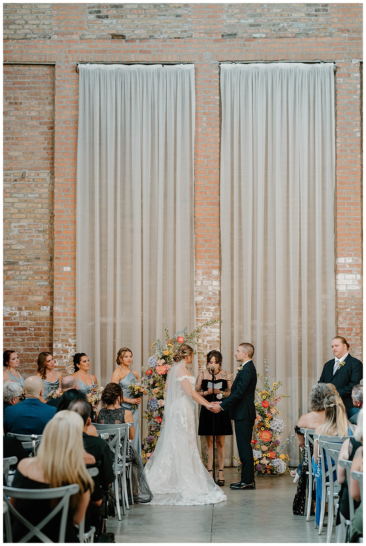 bride and groom hold hands at altar with colorful floral arch by Indigo Lace Collective