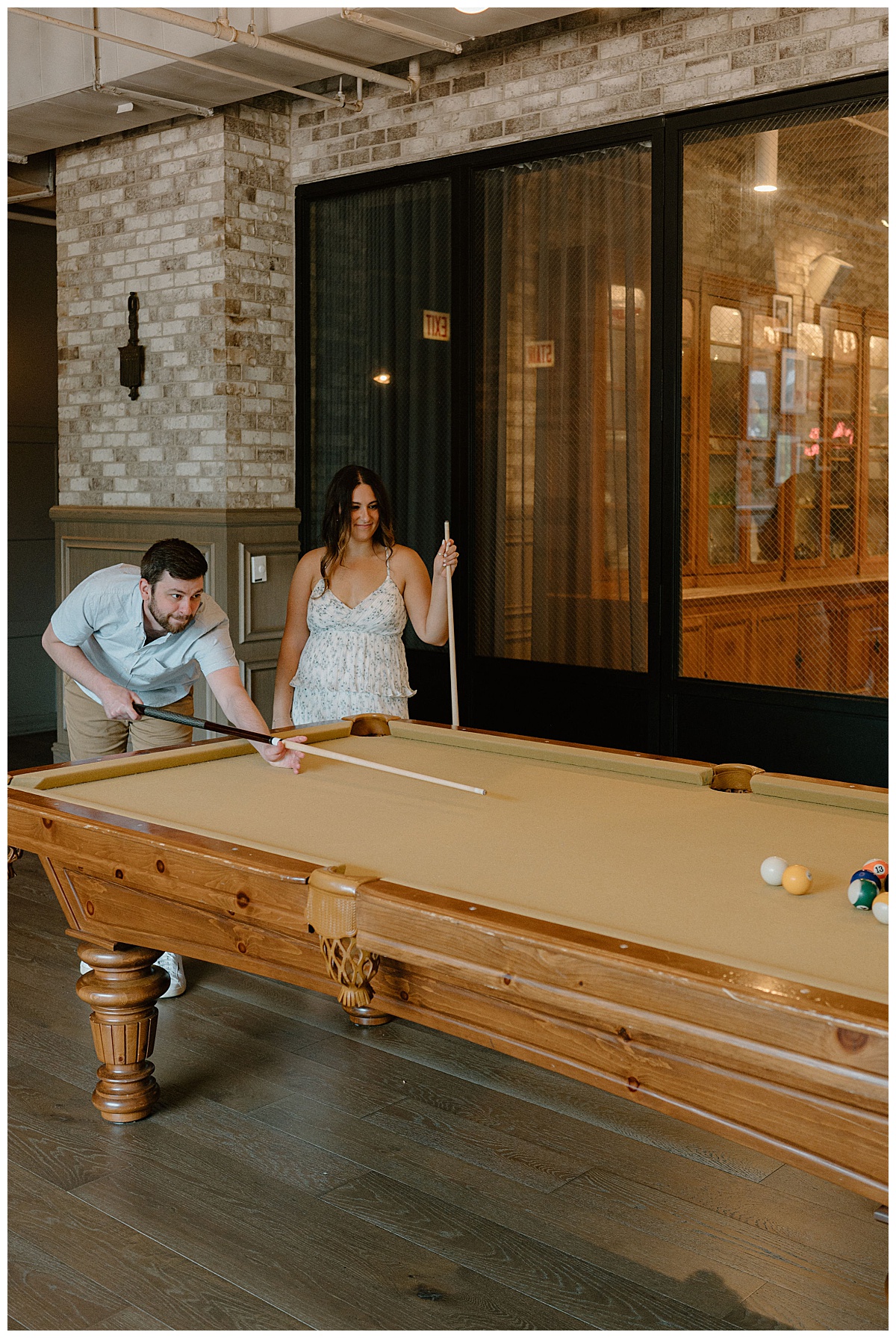 guy leans over pool table as girl watches by Chicago wedding photographer