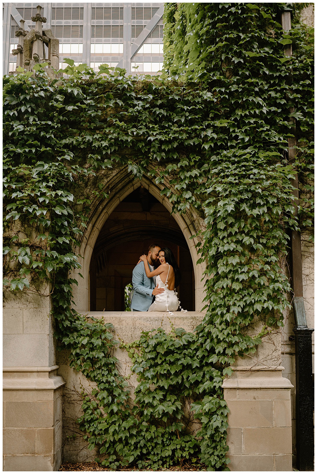 woman sits in archway while man hugs her waist by Chicago wedding photographer