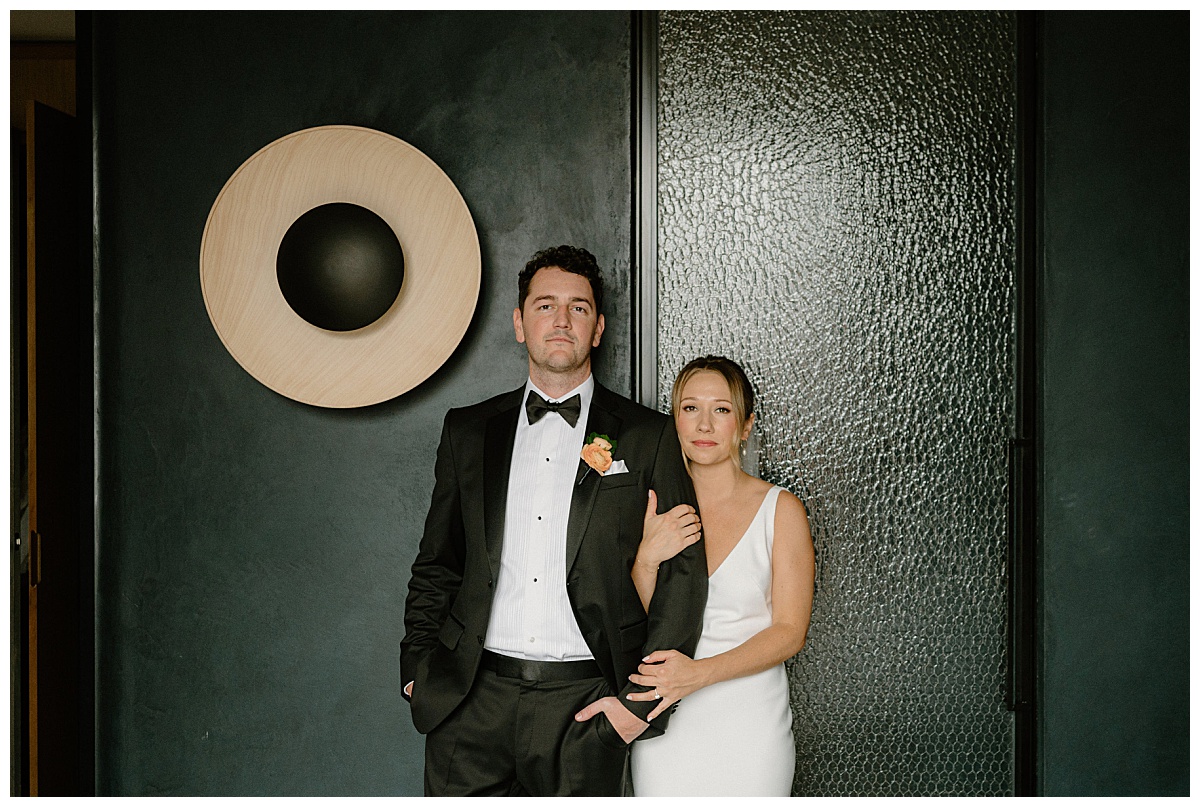 woman holds man's arm as they stand in front of dark wall by Midwest wedding photographer