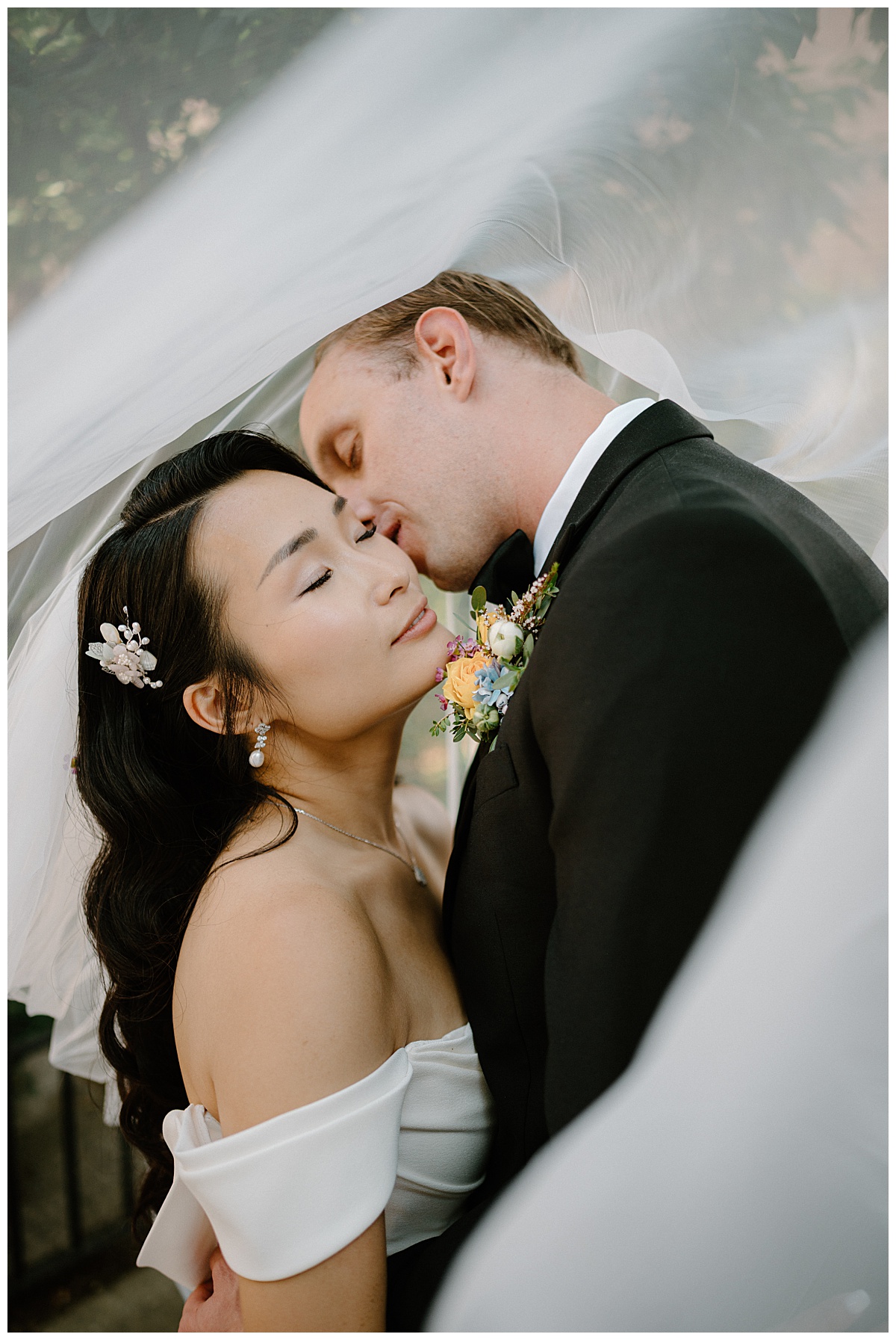 husband leans in to kiss wife's cheek under veil by  Indigo Lace Collective