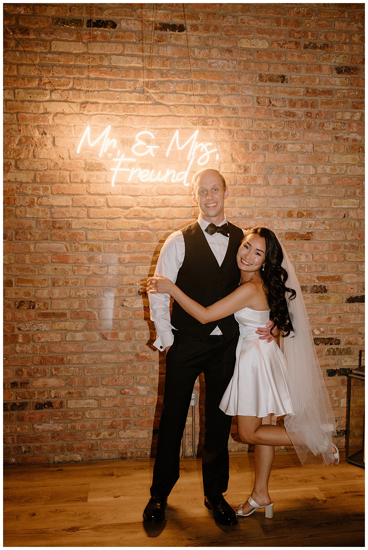 newlyweds hug under neon sign by  Indigo Lace Collective