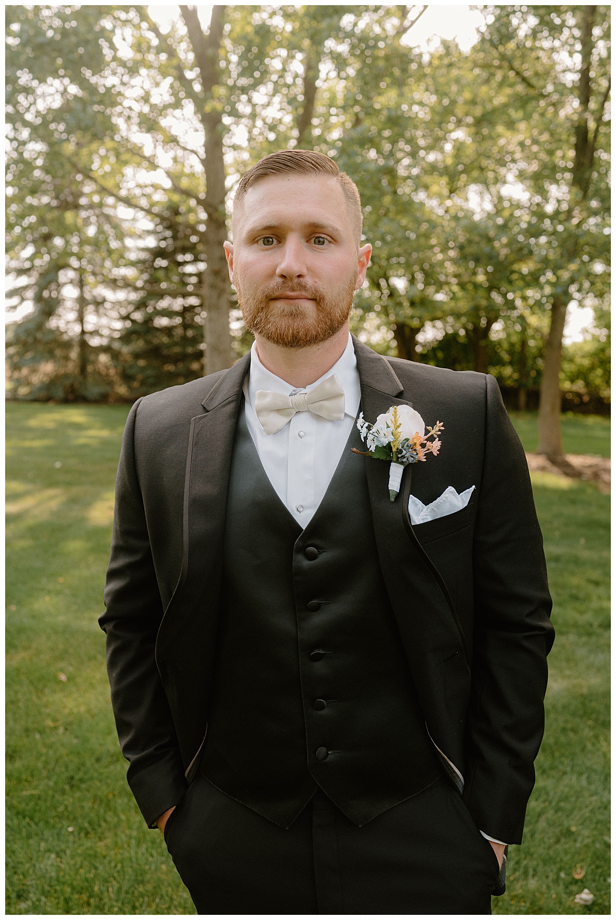 groom has hands in pockets and large trees behind him by Midwest wedding photographer