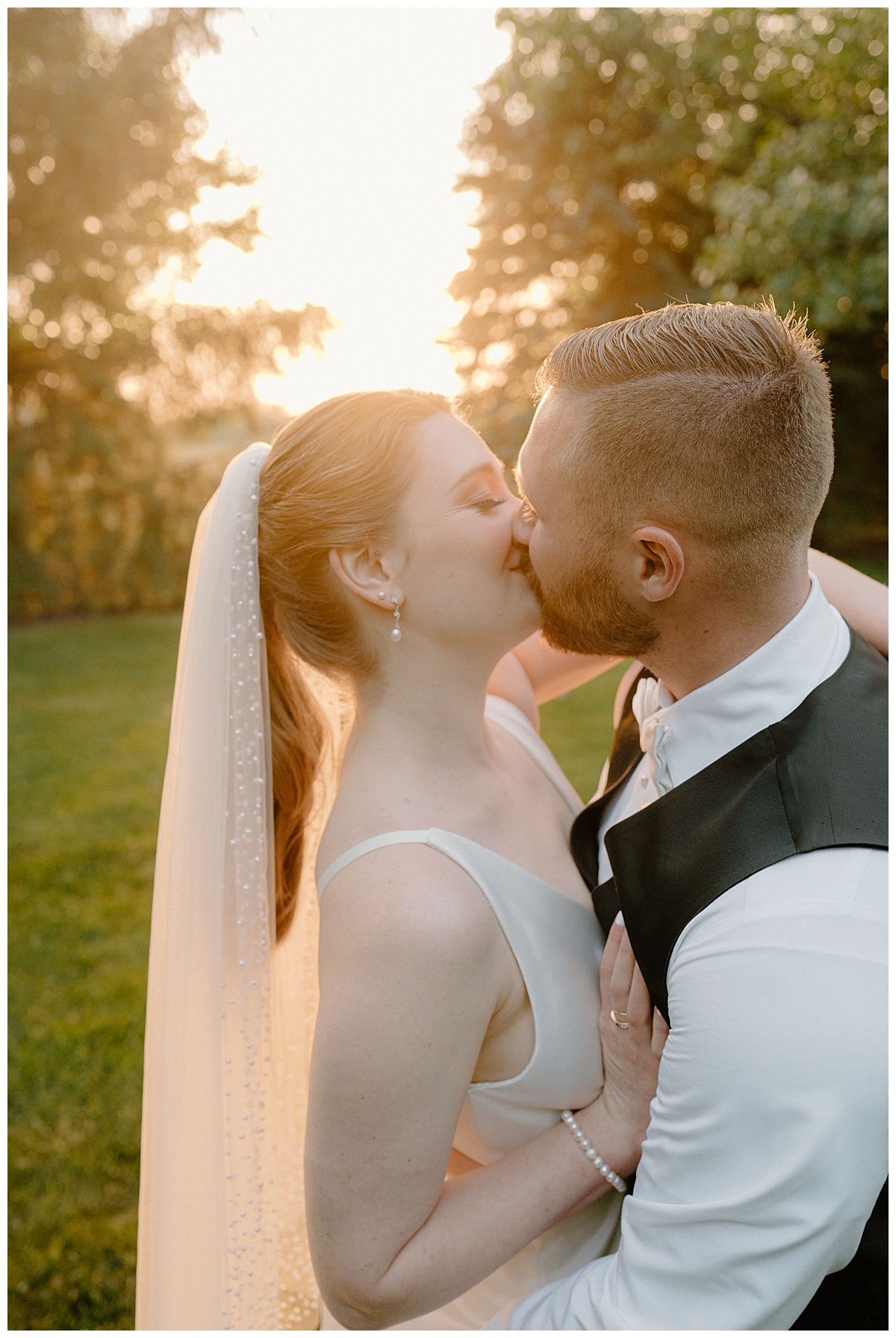bride and groom kiss during golden hour with sun shining behind during backyard summer celebration