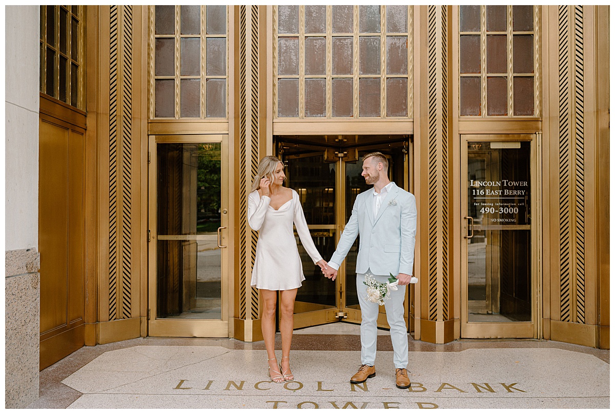 couple holds hands in front of gold gilded building at Downtown Fort Wayne Courthouse Elopement