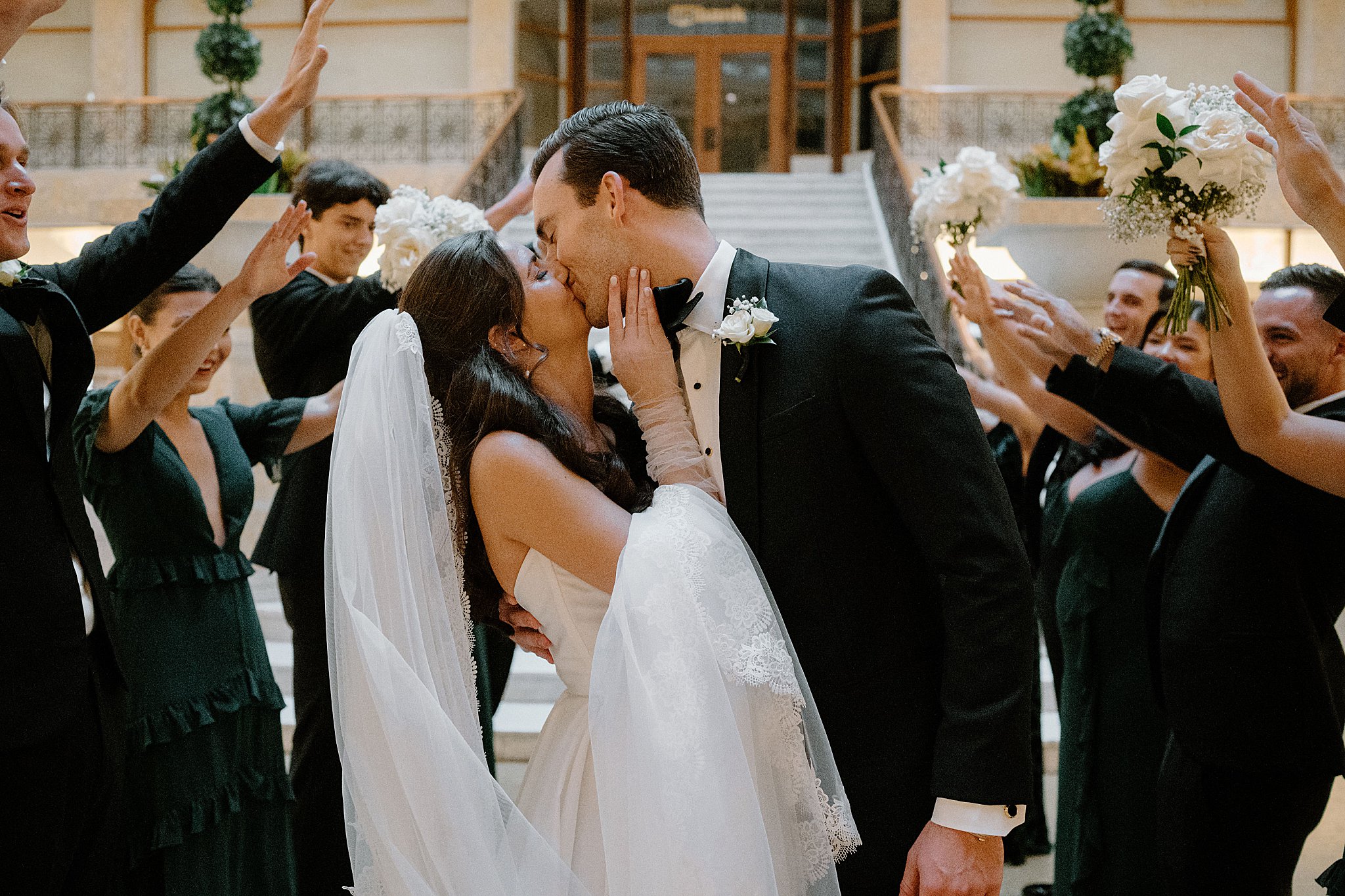 husband and wife share kiss in front of wedding party by Indigo Lace Collective