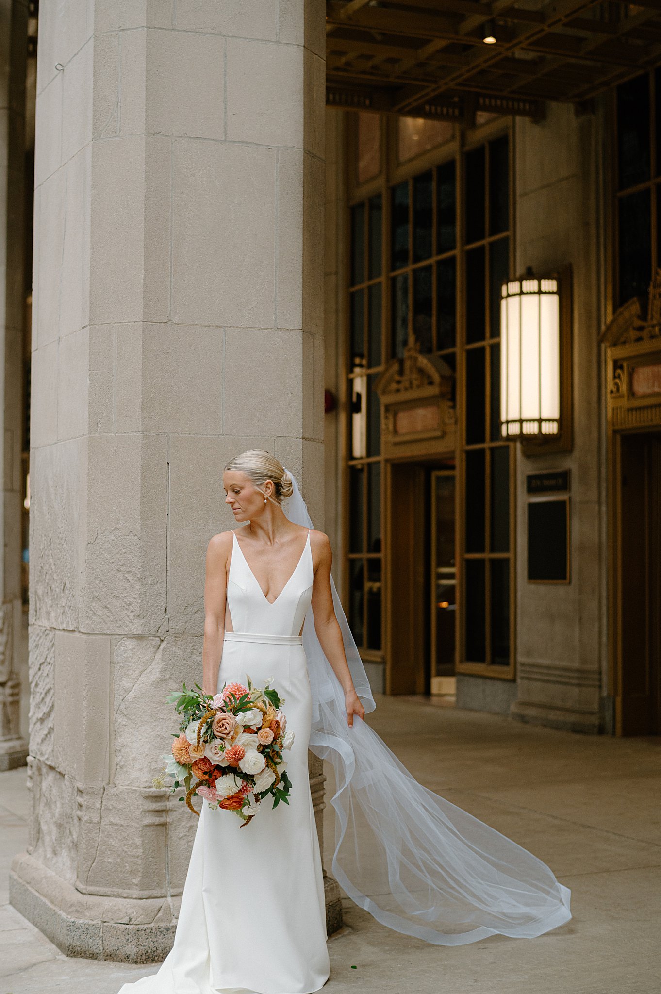 bride holds bouquet and veil as she looks over her shoulder by Chicago wedding photographer