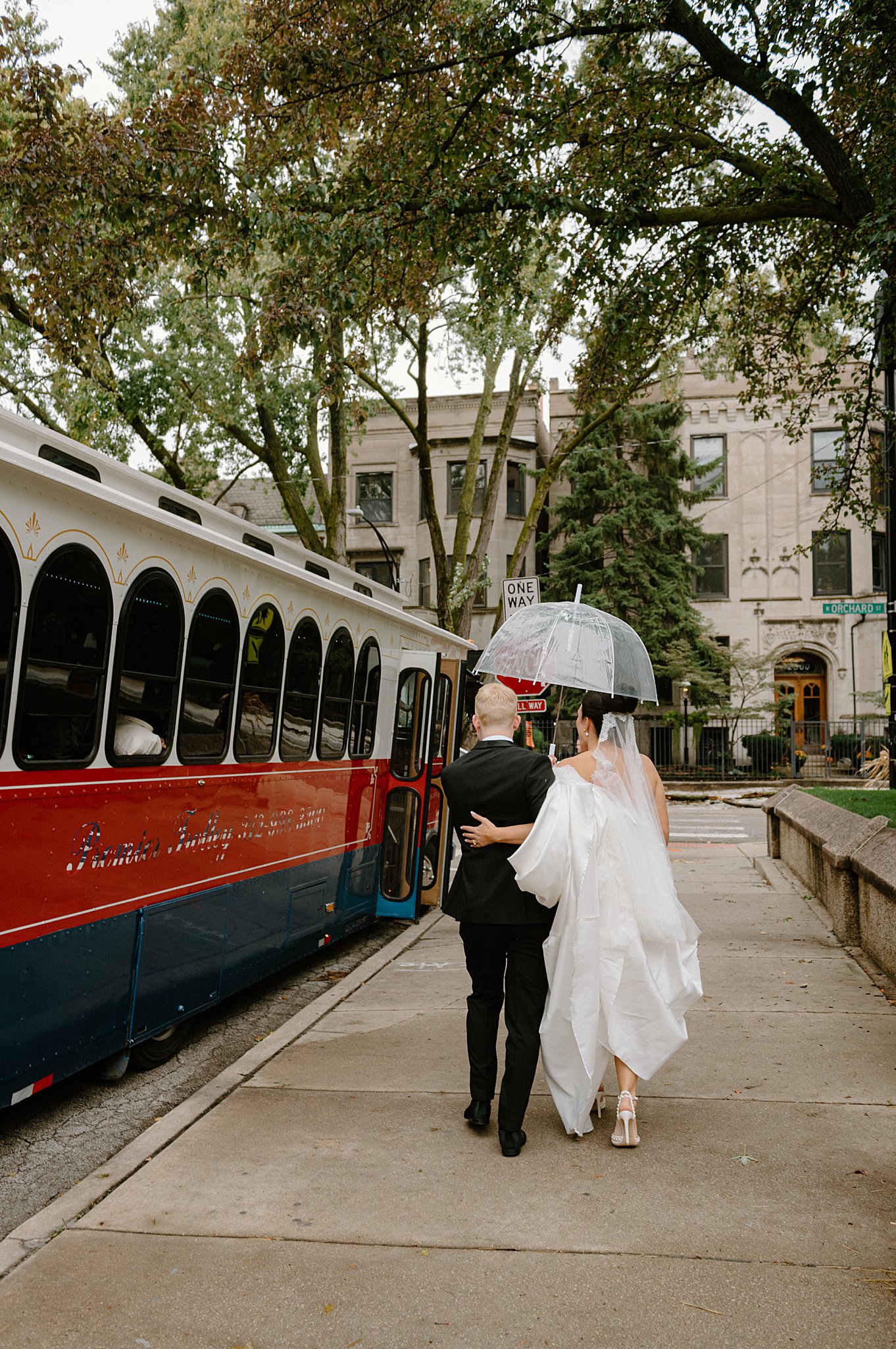 bride and groom walk to trolly holding umbrella by Midwest wedding photographer