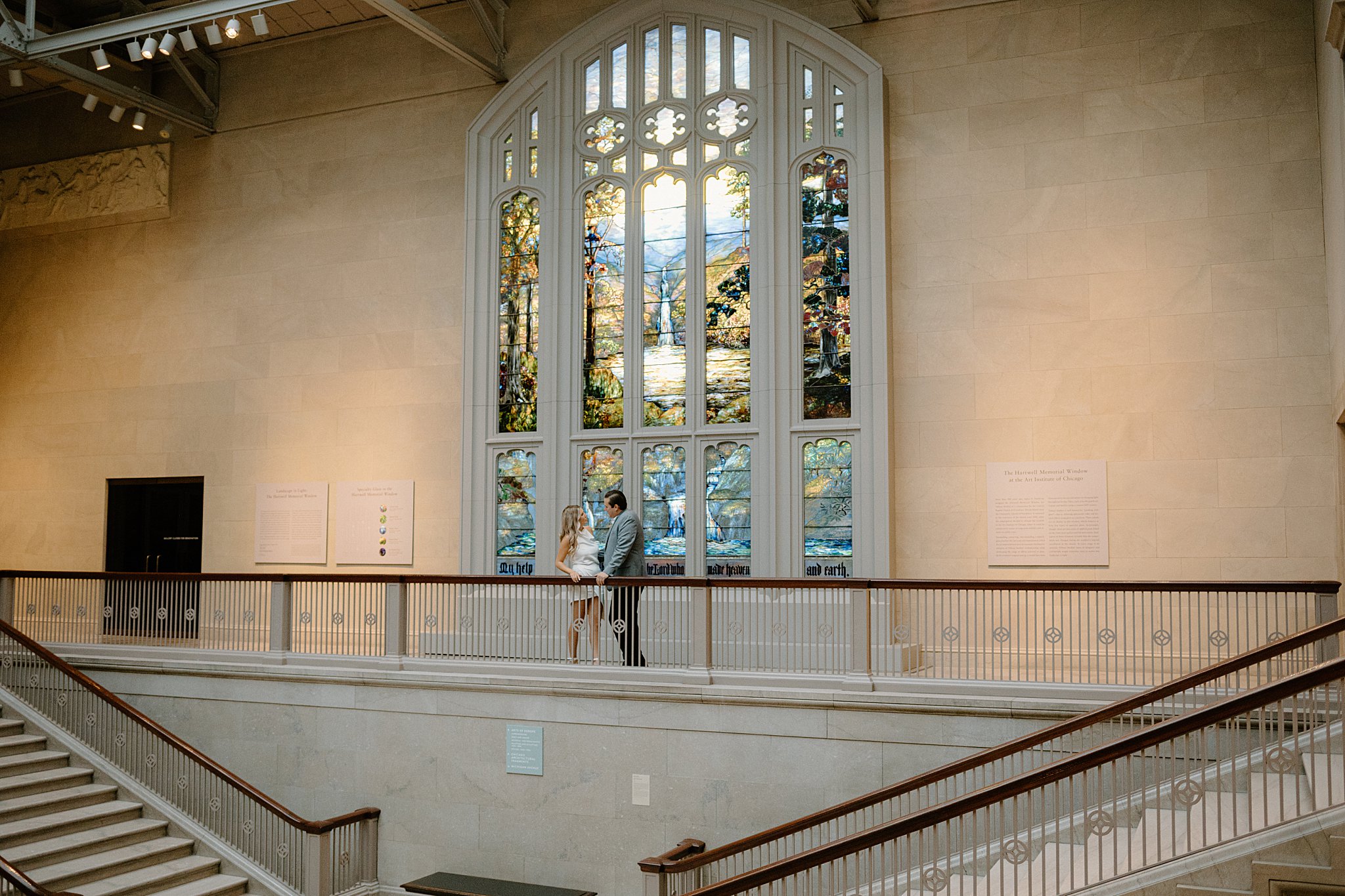 couple lean on railing in front of stained glass at Chic Art Institute Engagement Session