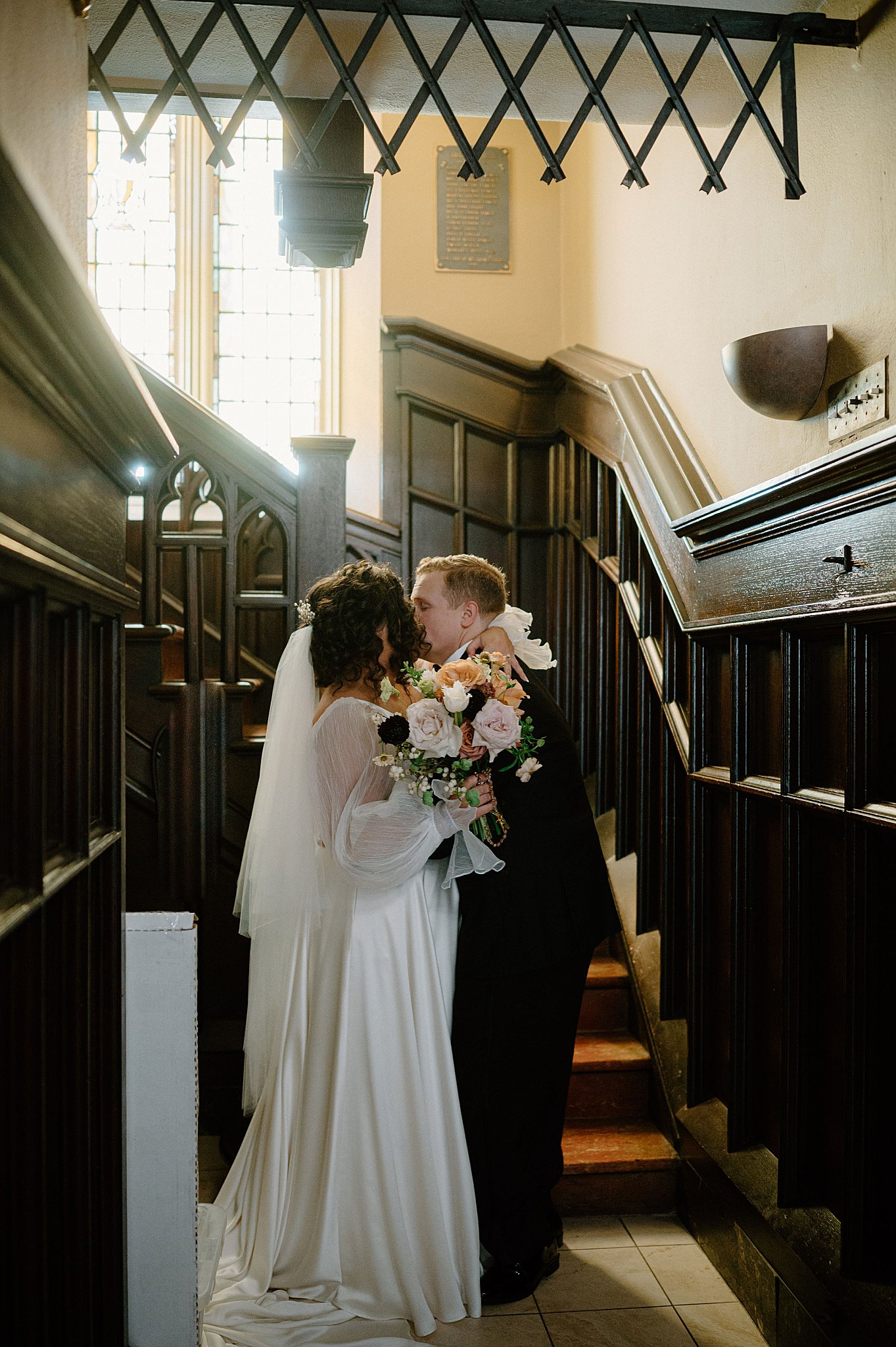 bride and groom steal a kiss in the stairwell of church by Indigo Lace Collective