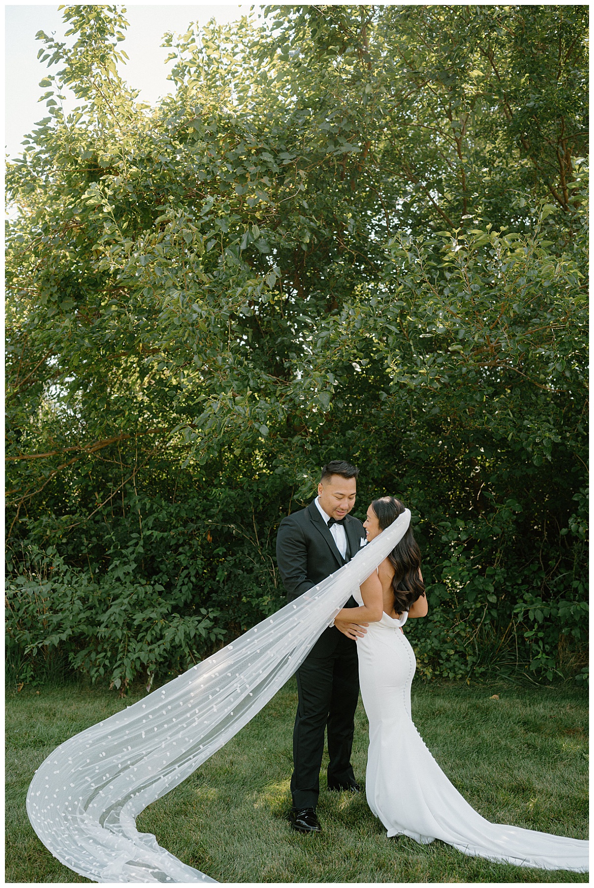 bride's veil blows dramatically in the wind as she stands with groom by Indigo Lace Collective